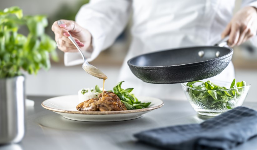 Female Cook Finishing Food With Sauce On Counter In Restaurant O